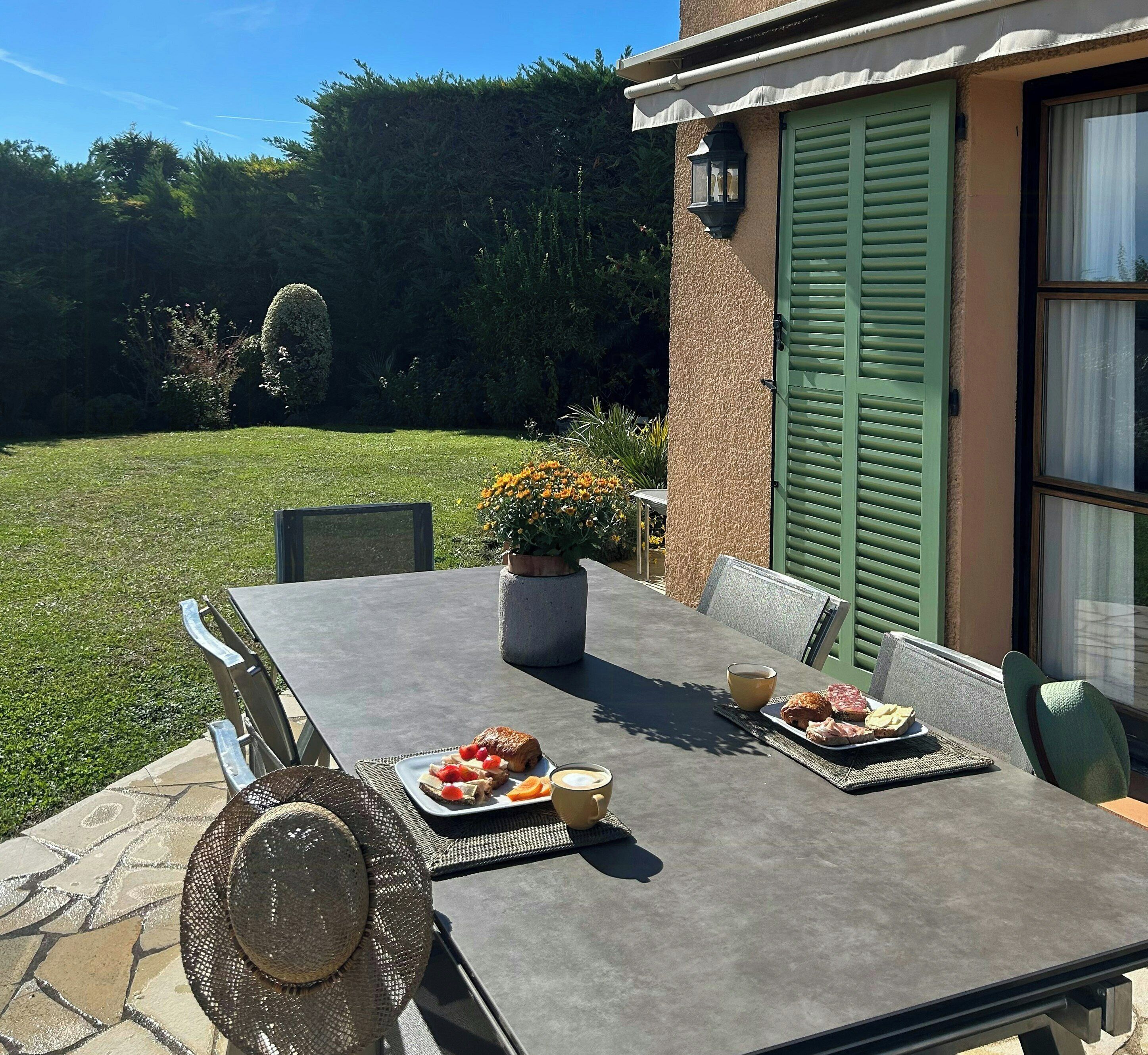 An outdoor dining table with chairs, a potted plant, and food items.