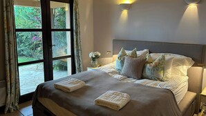 Une chambre à coucher avec un grand lit, deux lampes fixées au mur, une table de chevet et une fenêtre avec des rideaux.