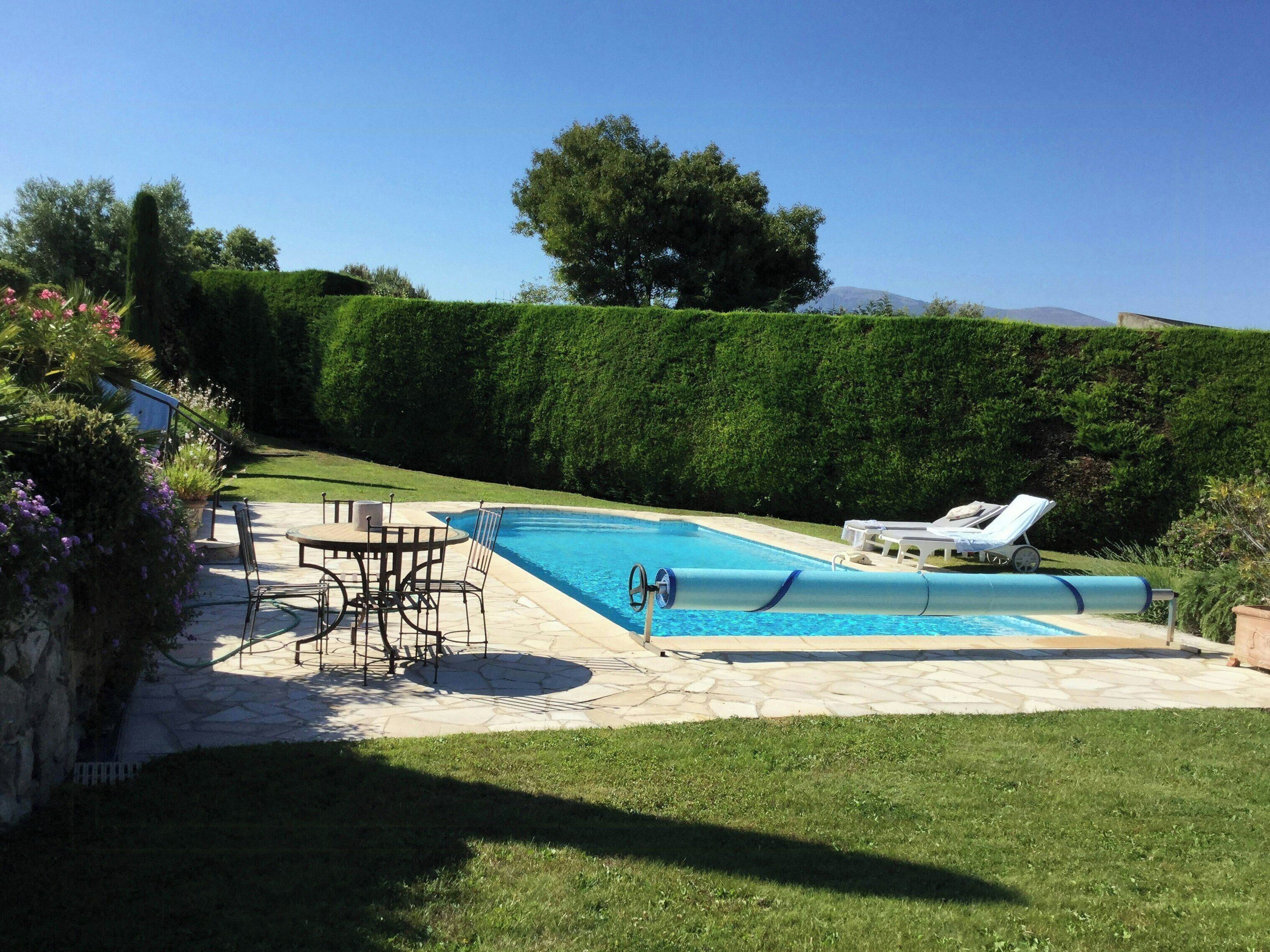 A swimming pool with a lounge chair, a table with chairs, and a well-maintained lawn.