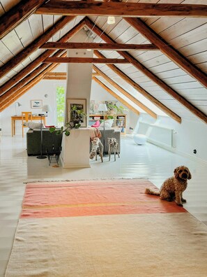 An attic room with a high ceiling, wooden beams, a desk, a chair, a sofa, a rug, and a dog. - Century-old house with sea views in Södra Mellby (Kivik)