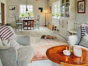 A cozy living room with a dog, a dining area, and a white cabinet with glass doors. - Century-old house with sea views in Södra Mellby (Kivik)