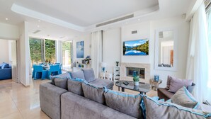 A modern living room with a grey sofa, blue chairs, a fireplace, and a large TV. - Lombardi Villa Protaras (Protaras)