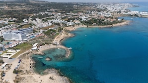 An aerial view of a coastal resort with a large hotel, clear blue waters, and a sandy beach. - Lombardi Villa Protaras (Protaras)