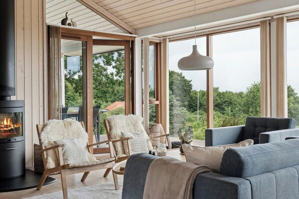 A modern living room with a fireplace, large windows, and comfortable seating. - Seaside cottage at Bønnerup Strand (Glesborg)