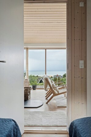 A room with a large window, a wooden floor, a white chair, and a view of the sea. - Seaside cottage at Bønnerup Strand (Glesborg)