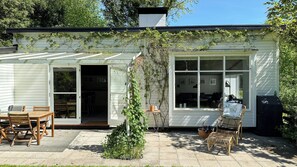 Ein Haus mit überdachter Terrasse, Essbereich mit Stühlen und einem Garten.