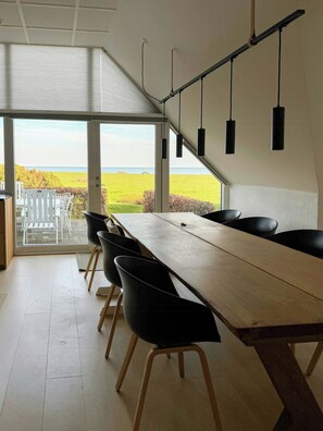 Een eetgedeelte met een lange tafel, zwarte stoelen en uitzicht op zee door grote ramen.