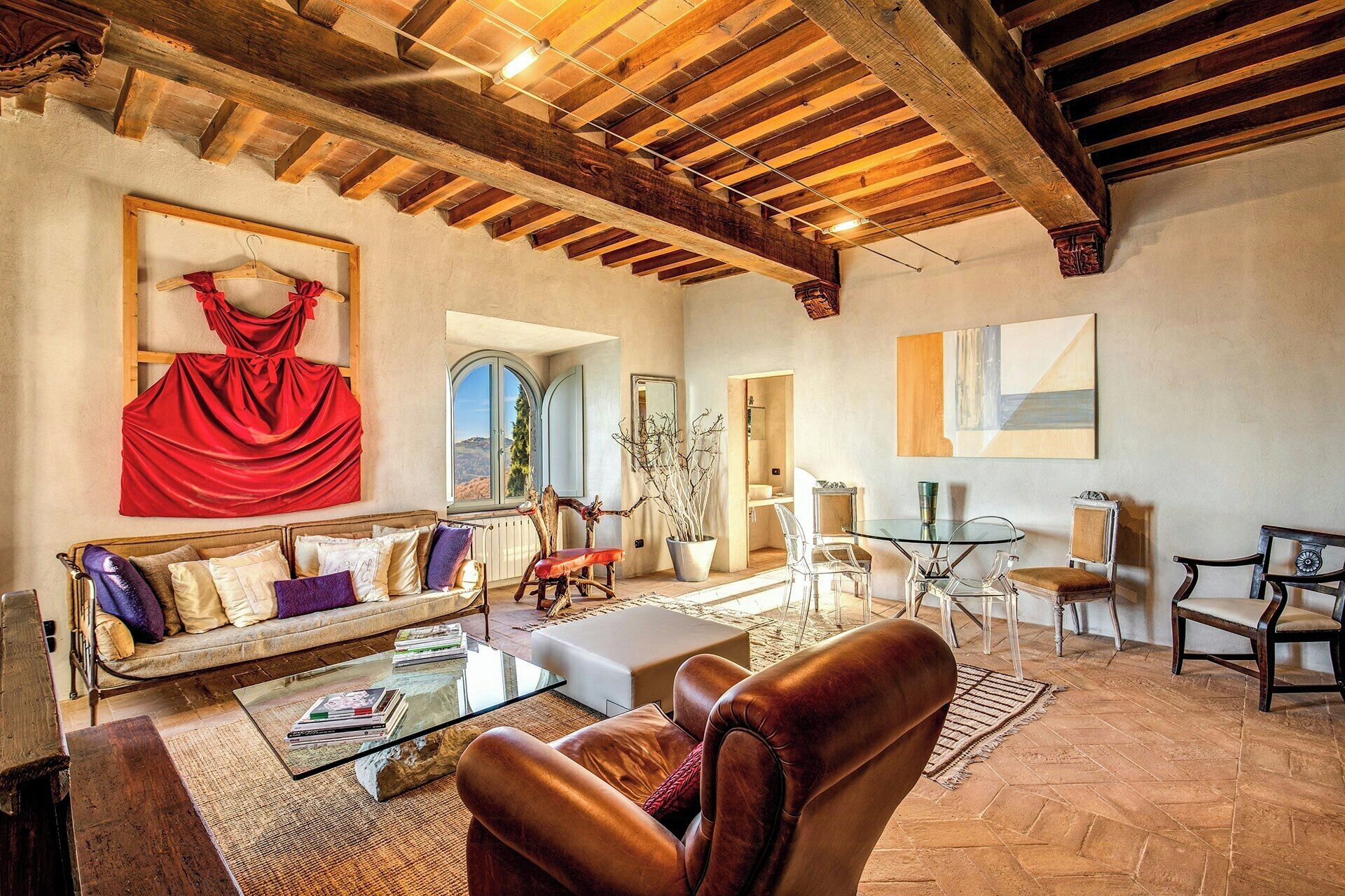 A spacious living room with a wooden ceiling, a sofa, a glass coffee table, and a leather armchair.