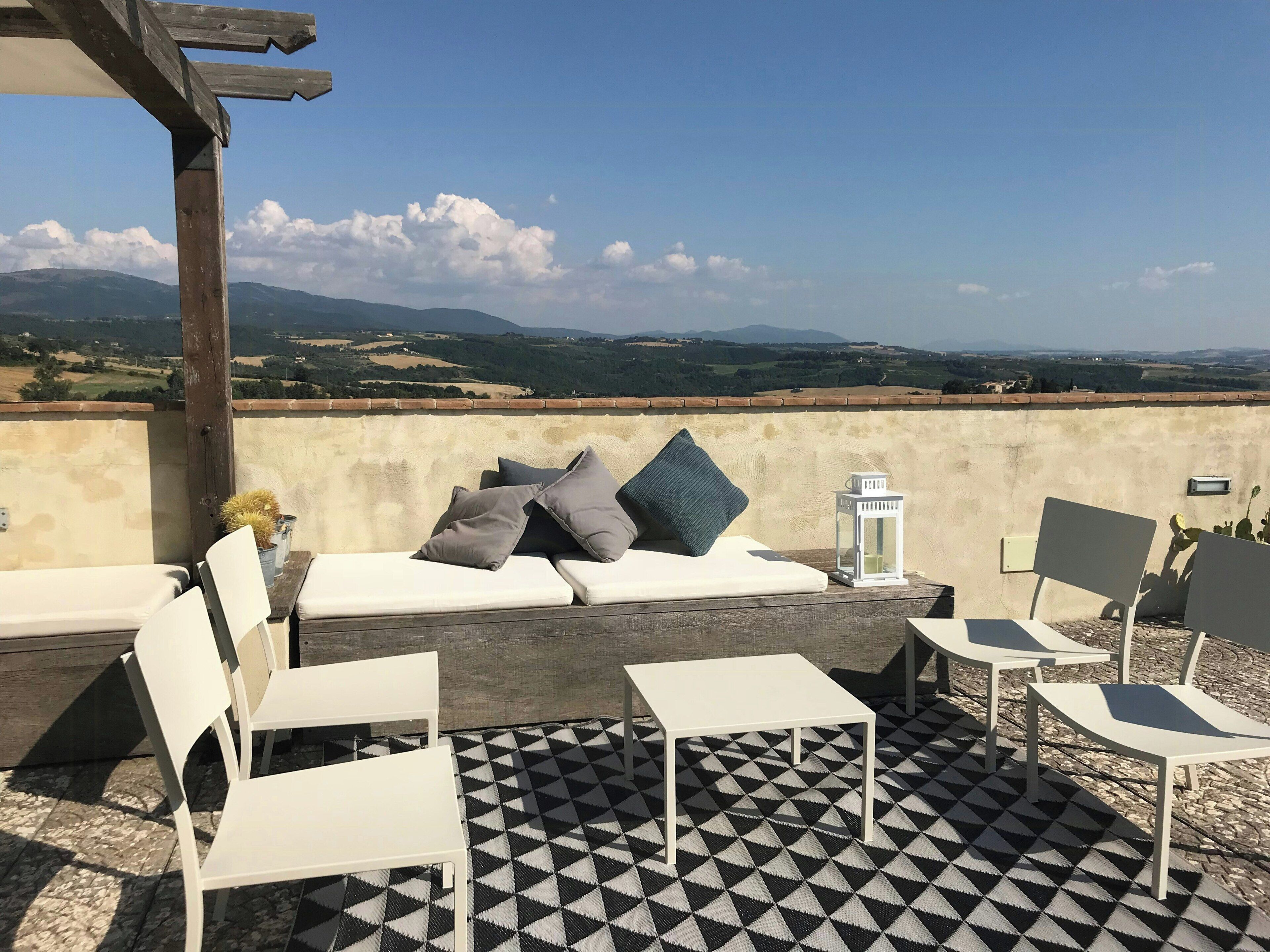 A terrace with a sofa, chairs, and a table, overlooking a scenic landscape.