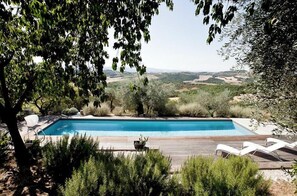 Ein rechteckiger Pool mit Holzterrasse, umgeben von Grün und mit Blick auf eine hügelige Landschaft.