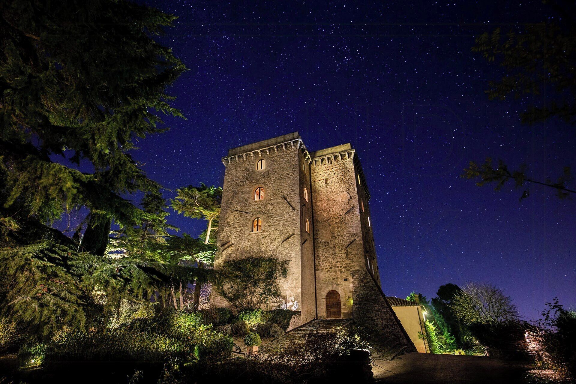 A historic stone tower with arched windows, surrounded by dense foliage.