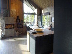 A modern kitchen with a stone fireplace, large windows, and a view of trees. - Family cabin with views of Store and Lille Hødn (Hemsedal)