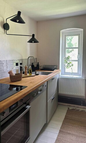 Eine Küche mit Holzarbeitsplatte, Spüle, Fenster mit Blick auf Grünflächen und einer Heizung.