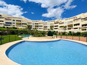 Ein Hotel mit Schwimmbad, mehreren Balkonen und blauem Himmel.