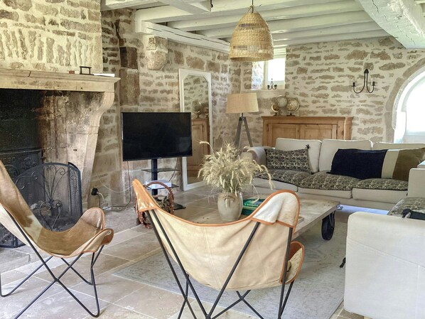 Ein rustikales Interieur mit Kamin aus Stein, einem Flachbildfernseher, einer Couch und einer Hängelampe aus Weidengeflecht.