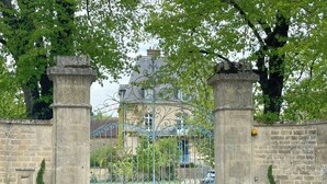Une entrée fermée par un portail en fer forgé, flanquée de piliers en pierre et agrémentée de plantes en pot.