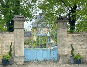 Ein verschlossener Eingangsbereich mit schmiedeeisernem Tor, Steinpfeilern und Kübelpflanzen.