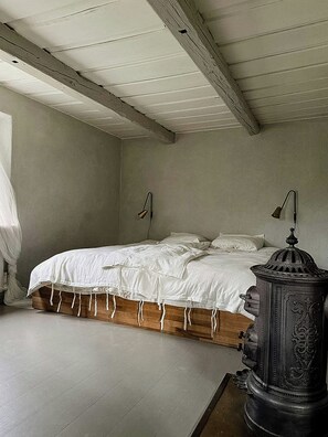 A bedroom with a wooden bed frame, white bedding, two wall-mounted lamps, and a decorative metal object on a table. - Framed structure with annexes in Österlen (Brösarp)