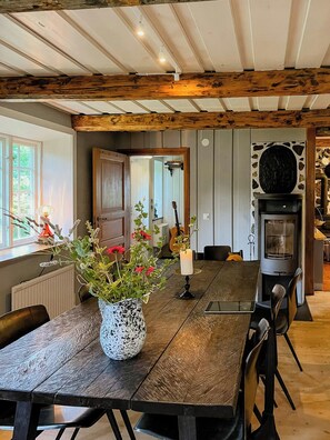 A dining area with a wooden table, chairs, a vase with flowers, a candle, and a fireplace. - Framed structure with annexes in Österlen (Brösarp)