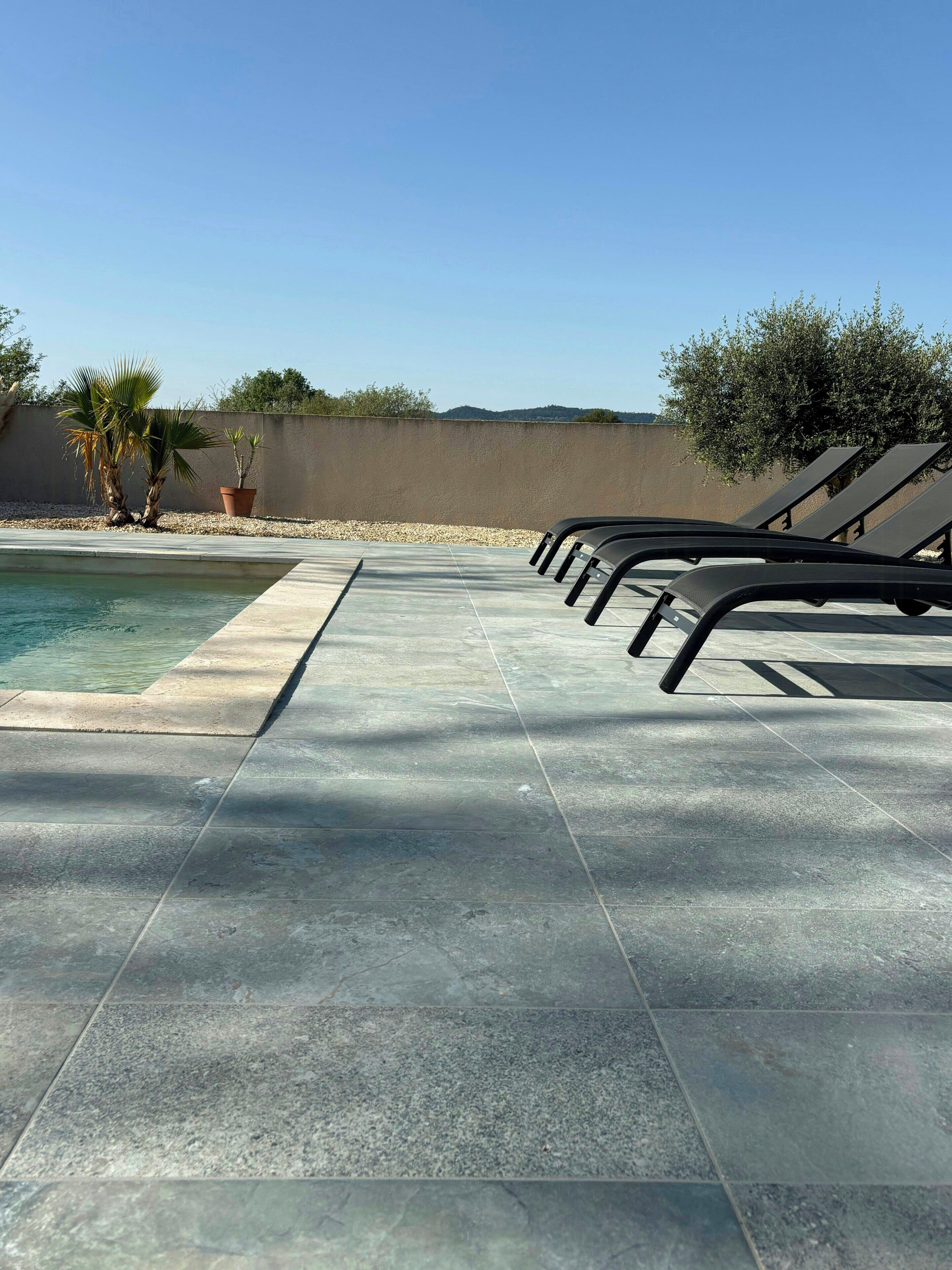 A poolside area with lounge chairs, a swimming pool, and potted plants.