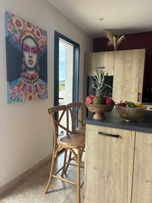 A kitchen with wooden cabinets, a chair, a fruit bowl, and a painting on the wall. - House with pool in the Cèze valley (Saint Gervais)
