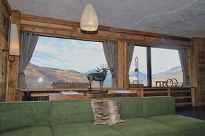 A room with a green sofa, a deer statue, and a large window with a mountain view. - Former hotel transformed into chalet in Valmorel (Les Avanchers-Valmorel)
