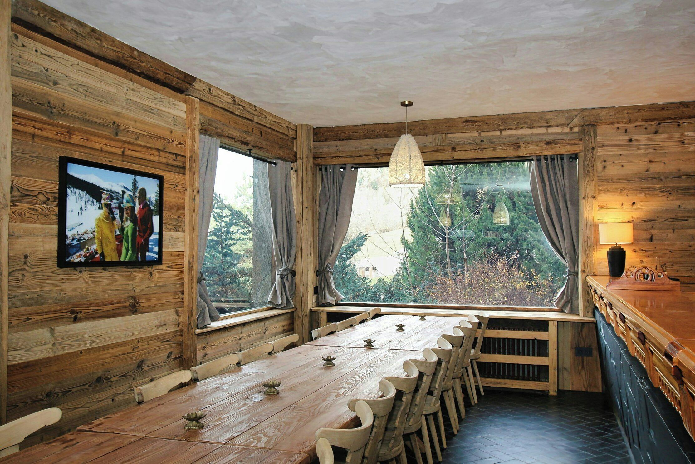 Ein Holzblockbau-Innenraum mit einem langen Esstisch, Stühlen, einem an der Wand befestigten Fernseher und einem Fenster mit Vorhängen.