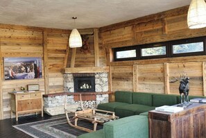 L’intérieur d’une cabane en rondins, avec une cheminée en pierre, un canapé vert, des meubles en bois et une sculpture de cerf accrochée au mur.