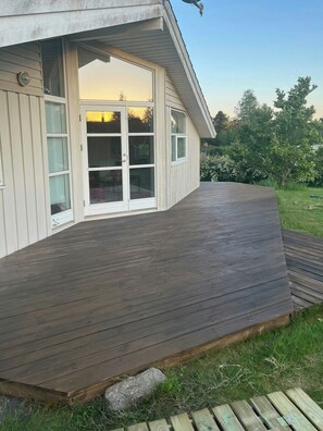 Une maison dotée d’une terrasse en bois, d’une porte-fenêtre coulissante et d’un petit jardin.
