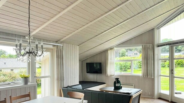 A room with a dining table, chairs, a TV, a sofa, and large windows offering a view of the outdoors. - Family retreat by Roskilde Fjord (Ølsted)