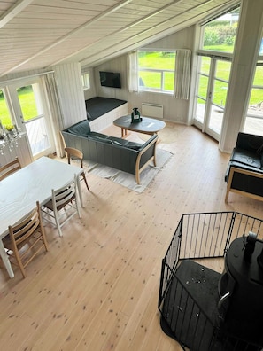 A spacious room with a dining table, a sofa, a small table with a chair, and a TV mounted on the wall.