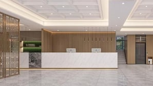 A modern hotel lobby with a reception desk, seating area, and a staircase leading to an elevator. - Starline Hotel (Dodoma)