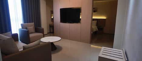 Una sala moderna con un sofá, una mesa de centro, un televisor de pantalla plana montado en un panel de madera, y una mesita con una lámpara.