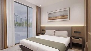A modern hotel room with a large bed, a city view through the window, a painting on the wall, and a nightstand with a lamp. - Starline Hotel (Dodoma)