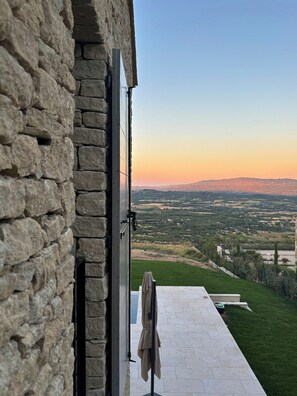 Eine Steinsicht mit einer Schiebetür, die auf eine Terrasse mit Blick ins Tal und auf ferne Hügel führt.