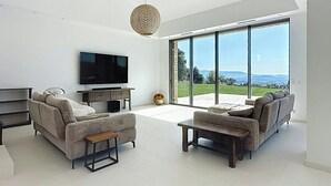 A modern living room with a flat-screen TV, two sofas, a coffee table, and a large window offering a view of the outdoors. - Villa with panoramic views and pool in Gordes (Gordes)