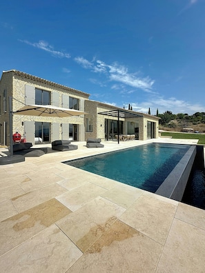 Ein zweistöckiges Steinhaus mit Swimmingpool, Außenbereich zum Sitzen und einer überdachten Terrasse.