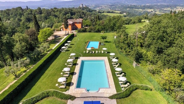 Un espace piscine comprenant deux piscines rectangulaires, entourées de chaises longues et de parasols, aménagé dans un cadre verdoyant luxuriant avec vue sur des collines lointaines.