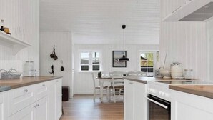 Cocina con armarios blancos, encimera de madera, lámpara colgante y ventana con vistas.