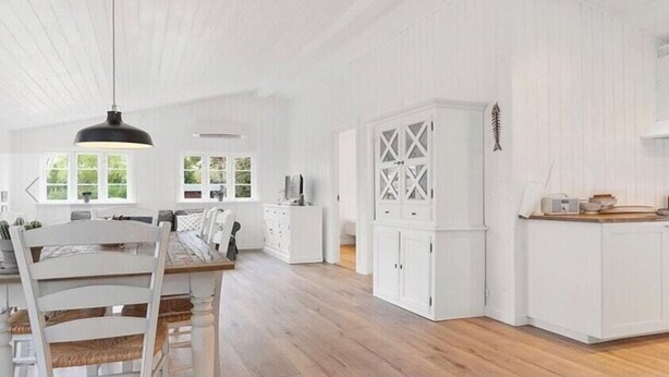 Una cocina amplia con armarios blancos, un comedor con mesa y sillas de madera, y un gran ventanal que proporciona luz natural.