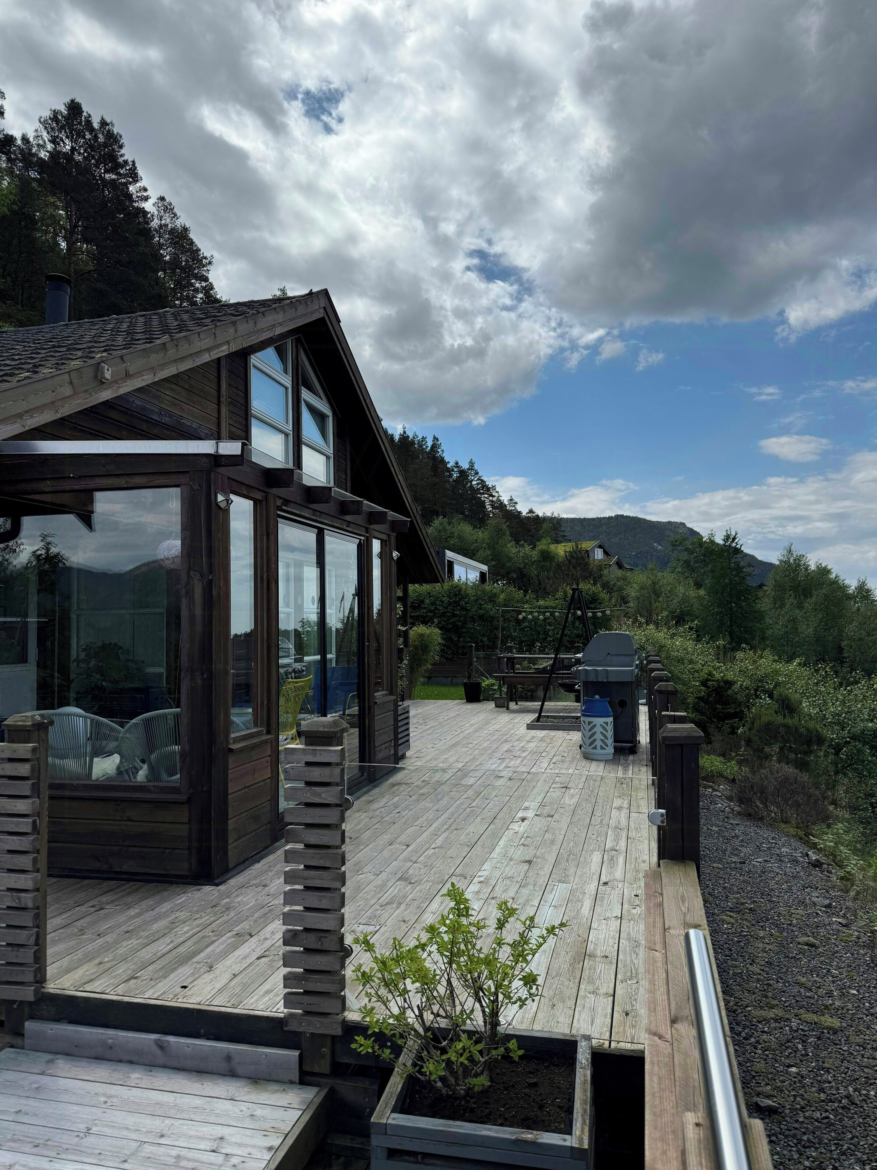 A modern wooden deck with a glass-enclosed room, a small garden area, and a view of the surrounding landscape.