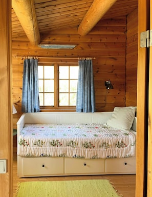 Un dormitorio de cabaña de madera con cama, cortinas, ventana y radiador.