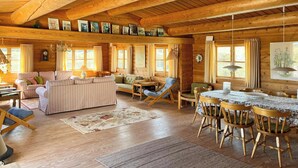 Een gezellig interieur van een blokhut met houten plafond, een zithoek, een eettafel met stoelen en een open haard.