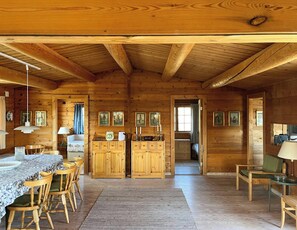 Interior de una cabaña de madera con comedor, armarios de madera y un pasillo que conduce a otra habitación.