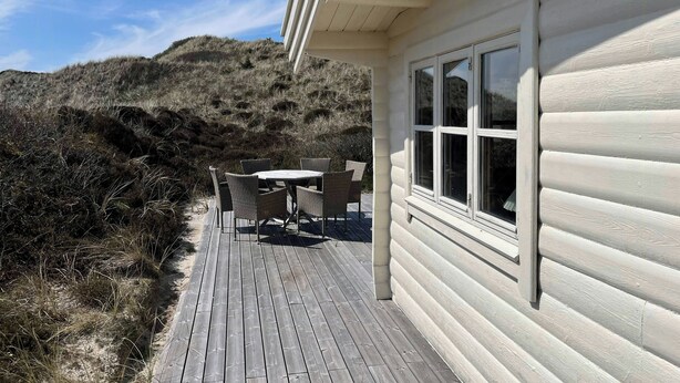 Een houten terras met een tafel en stoelen, uitkijkend op een glooiend landschap.