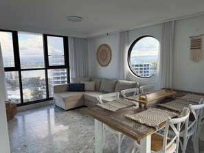 A modern living room with a large window, a round table, and a sofa. - Beachside Escape, VIEWS all around, steps to beach (Surfers Paradise)