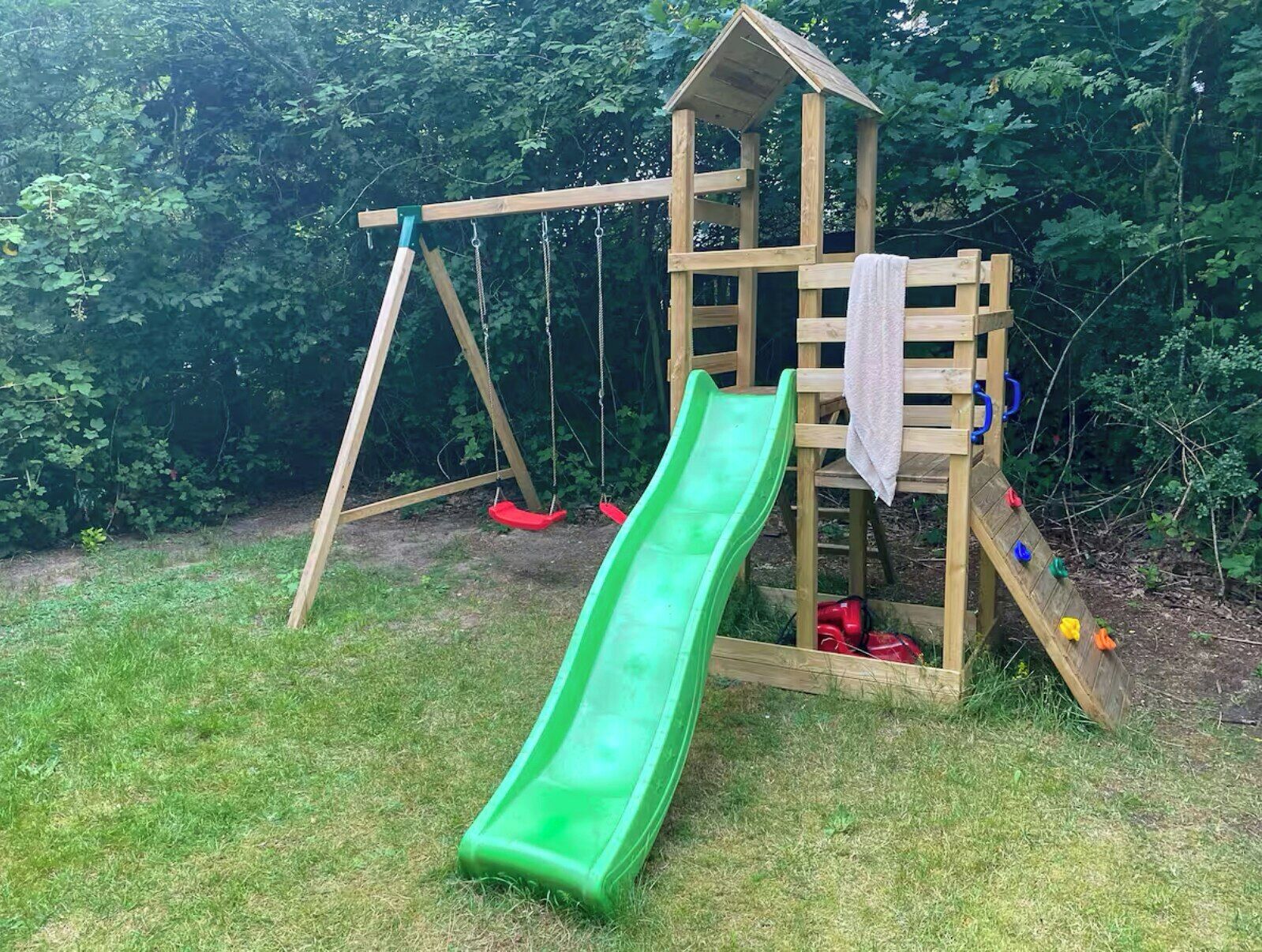 Una estructura de juego de madera con tobogán y columpios en un césped.