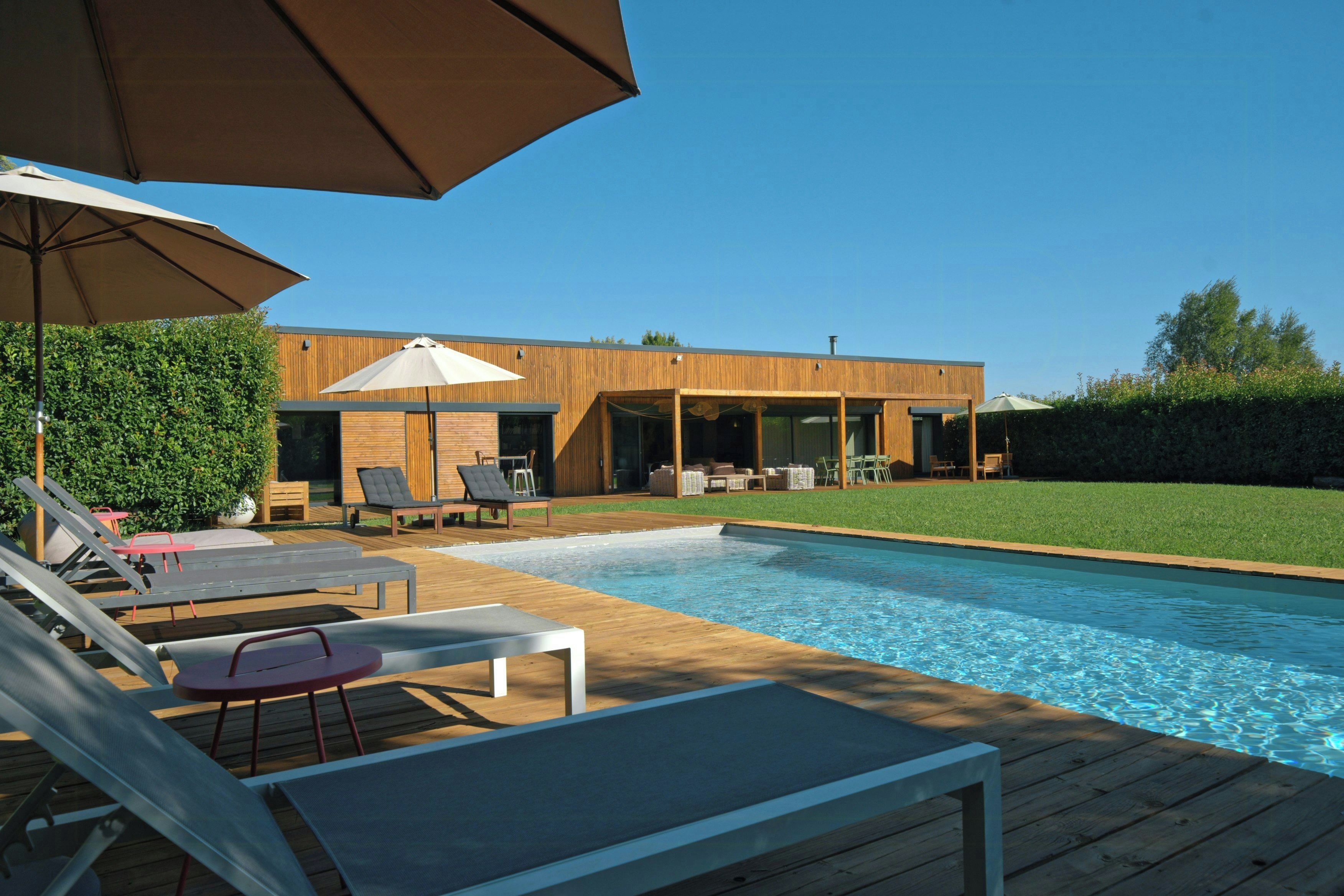 Un área de piscina moderna al aire libre con sillones de descanso y sombrillas.