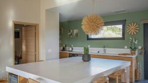 Une cuisine moderne dotée d’un grand îlot central, de chaises en bois, d’un luminaire suspendu et d’une fenêtre offrant une belle vue.