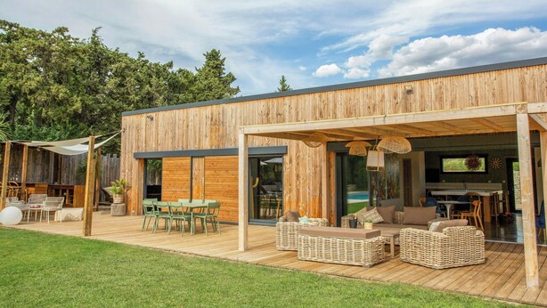 Une maison moderne en bois dotée d’une terrasse, d’un espace salon extérieur et d’une piscine.
